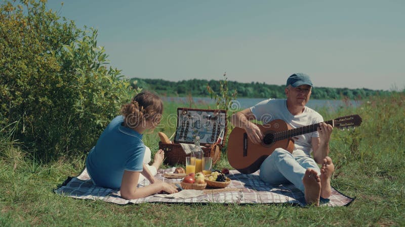 A woman and a man relax on a picnic and play the guitar.