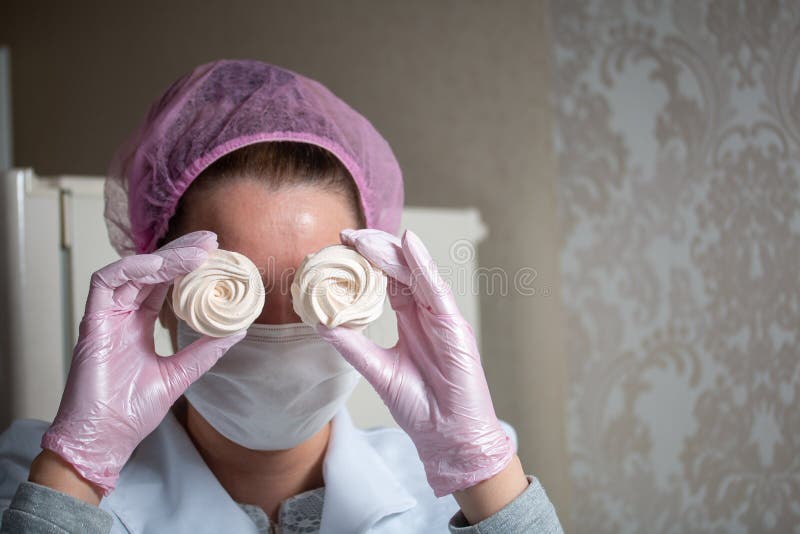 A woman in a mask and gloves holds fresh marshmallows in her hands. Cooking zephyr at home