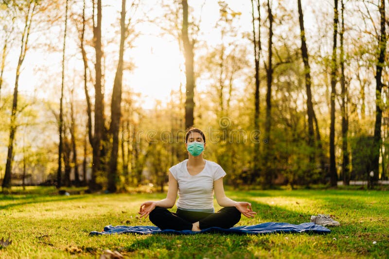 Woman with mask meditating in nature alone.Social distancing and active healthy lifestyle. Mindfulness meditation practice.