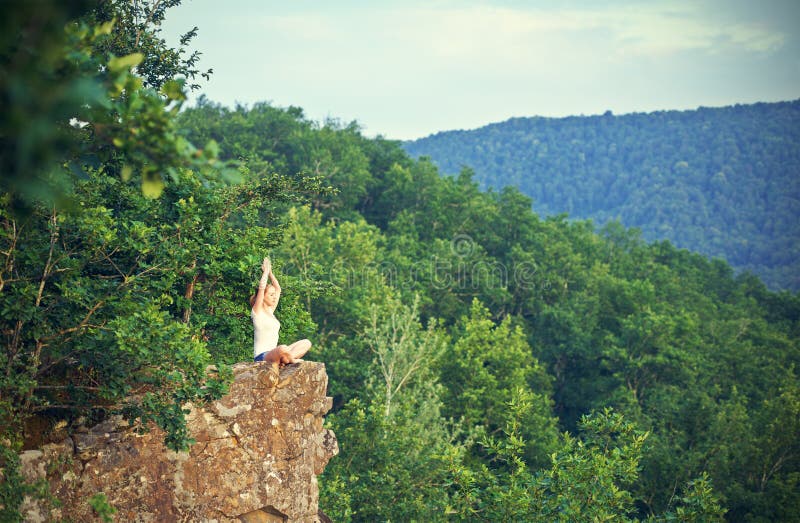 Woman meditating in lotus posture, doing yoga on top of the mountain