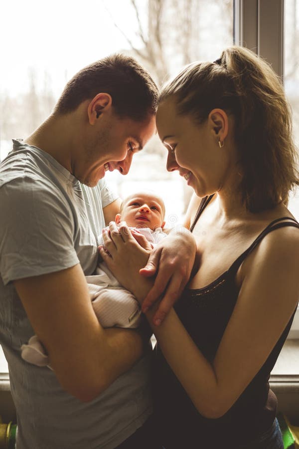 Woman and man holding on hands a newborn. On the background window. Mom, dad and baby. Portrait of young family. Happy family life