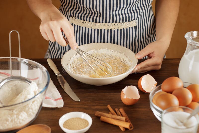 Woman mixes flour with eggs and milk in ceramic bowl on the kitchen.