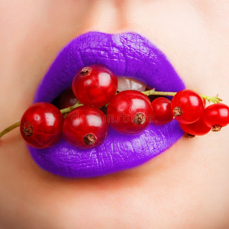 woman mouth with violet lips closeup holding a red currant