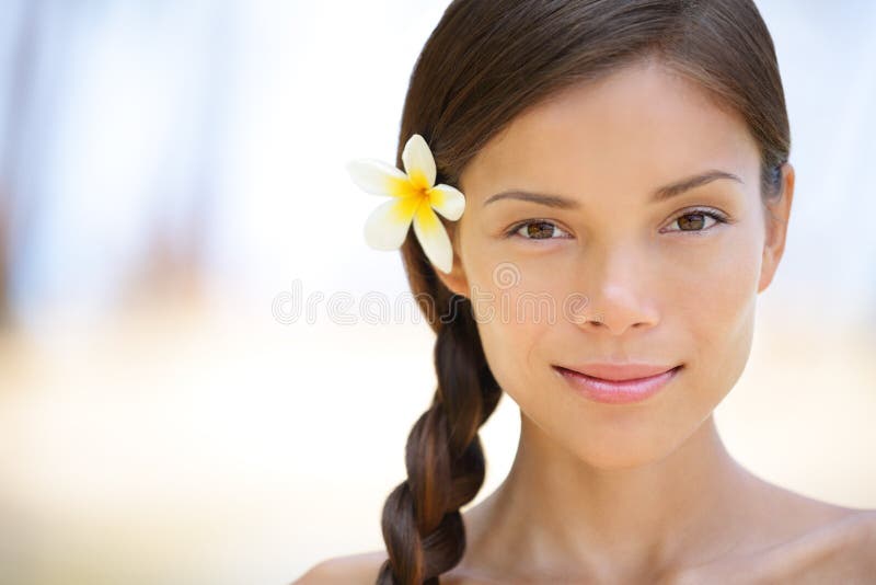 Woman natural beauty portrait of a beautiful and smiling brunette smiling outdoors with a flower in her braided hair. Multicultural Asian / Caucasian girl on health spa wellness travel resort