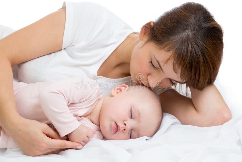 Woman and newborn boy relax in a white bedroom. Young mother kissing her newborn child. Mom nursing baby.