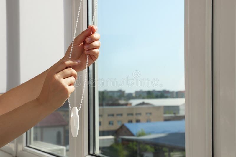 Woman opening blinds on window indoors, closeup. Space for text