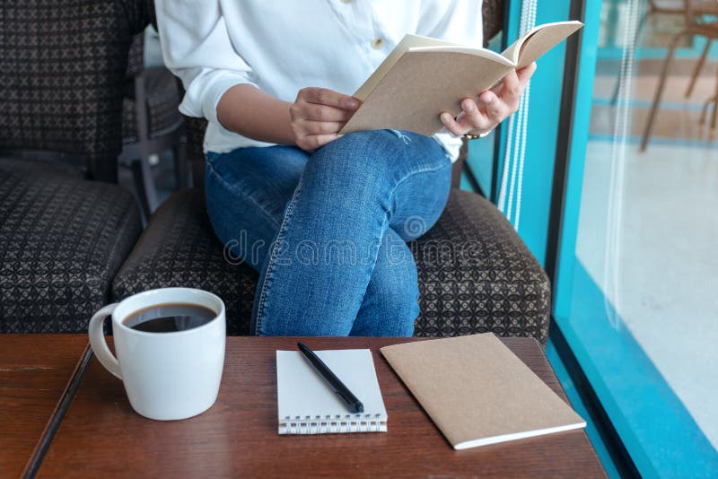 A woman opening a book to read with notebooks and coffee cup on wooden table in cafe