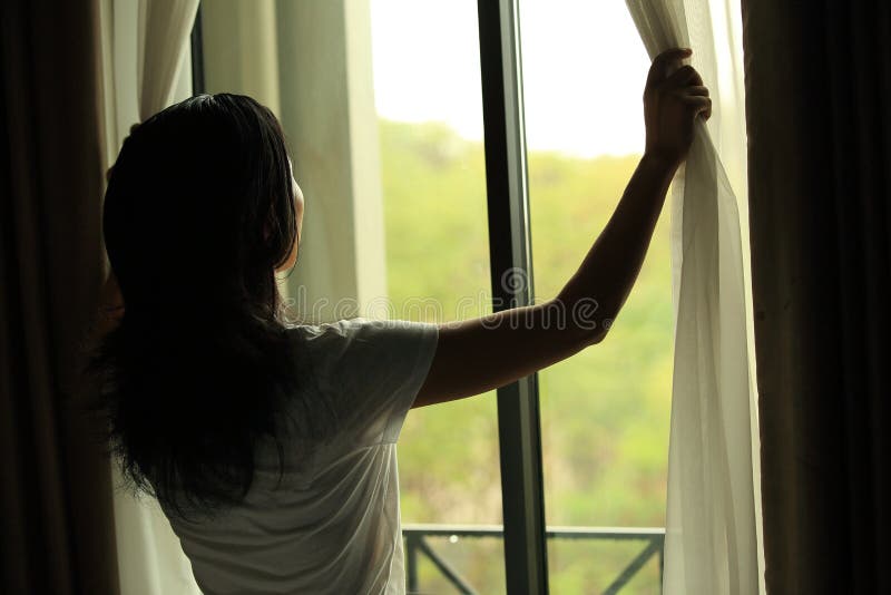 Young woman opening curtains in a bedroom morning after rain