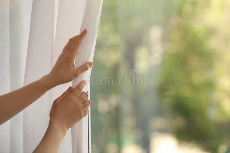 Woman opening white window curtains in room, closeup. Space for text