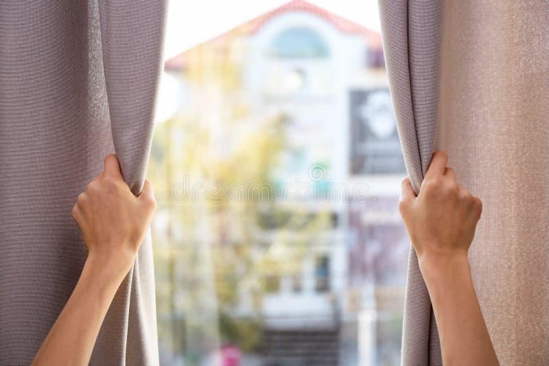 Woman opening window curtains at home, closeup. Space for text