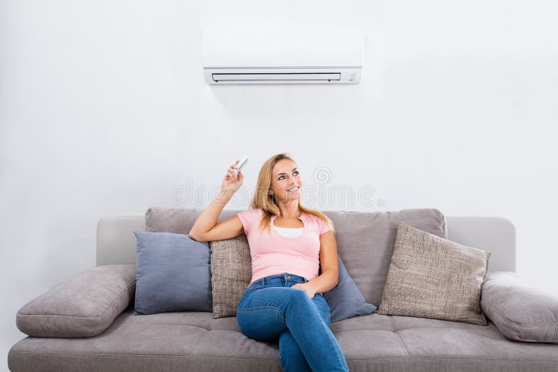 Woman Operating Air Conditioner With Remote Control
