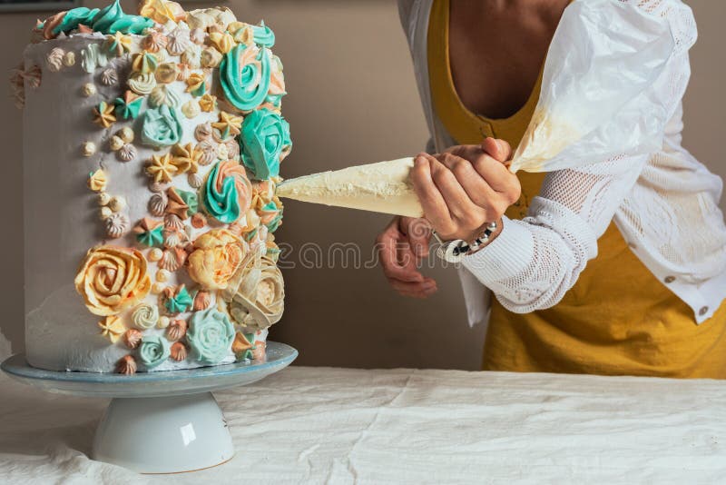 Woman pastry chef decorating a cake with a pastry bag with cream