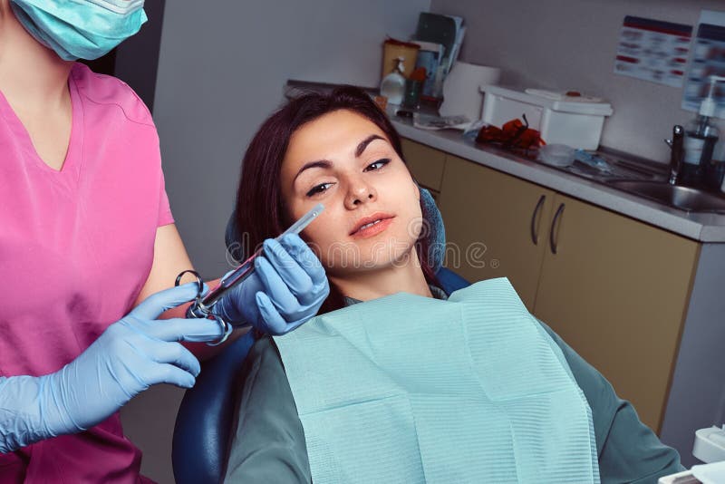 Woman Patient Sitting In A Dentist Chair While Her Doctor Preparing For Syringe Injection Stock