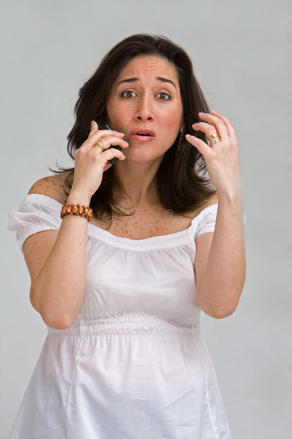 A beautiful latina lady dressed in white arguing on a cell phone, isolated on gray. A beautiful latina lady dressed in white arguing on a cell phone, isolated on gray