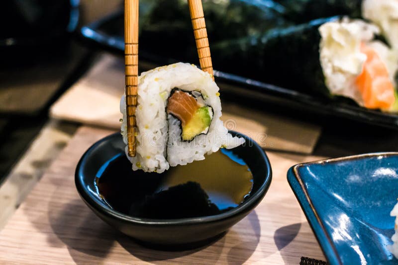 Woman picks up Uramaki sushi roll with fresh salmon, avocado and philadelphia cheese, covered with sesame seeds