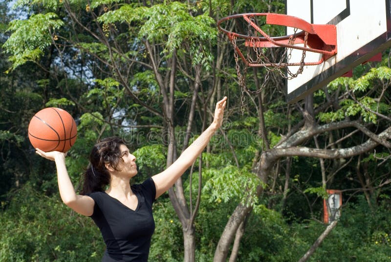 A woman is playing basketball on a court at the park. The woman is looking at the basketball hoop and about to make a shot. Horizontally framed photo. A woman is playing basketball on a court at the park. The woman is looking at the basketball hoop and about to make a shot. Horizontally framed photo.