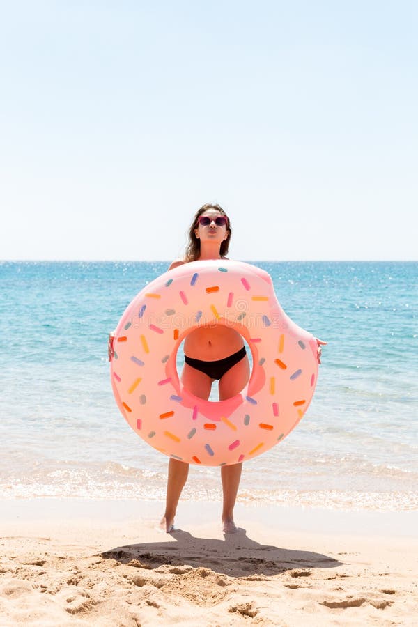 Woman playing with inflatable ring. Girl relaxing on pink inflatable on the beach. Summer holidays and vacation concept on a