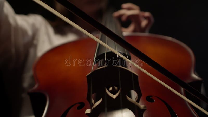 Woman playing violoncello closeup. Professional plays classical music on cello alone in the dark. Woman plays classical stock footage