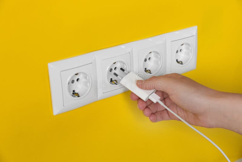 Woman Plugging Charger into Power Socket on Yellow Wall, Closeup