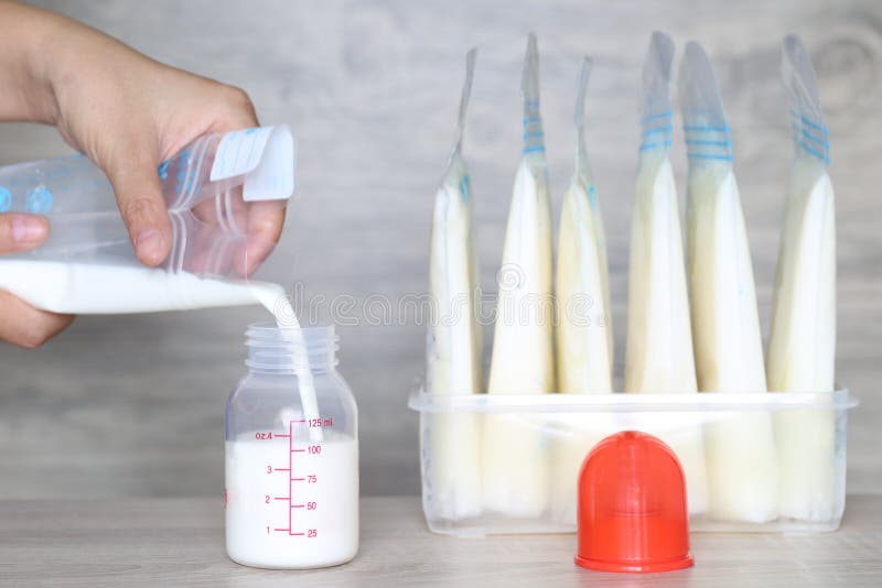 Woman pouring milk in to bottles for new baby on wooden table