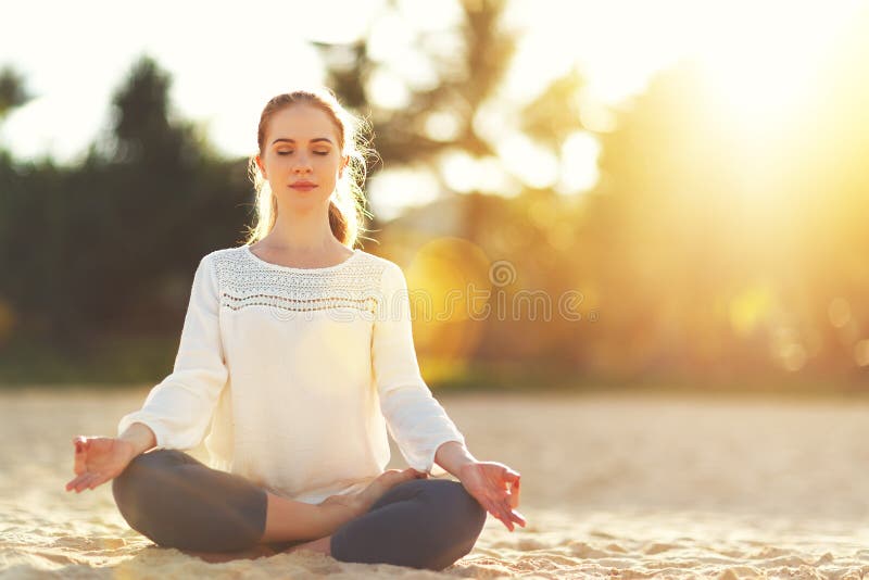 Woman practices yoga and meditates in lotus position on beach stock photos Woman practices yoga and meditates in lotus position on beach stock photos