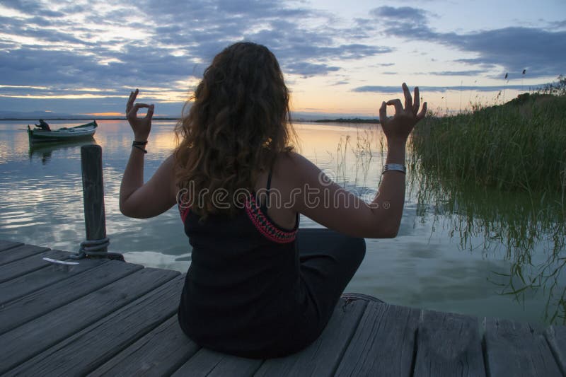 Woman practicing meditation in the lotus yoga position on a wooden jetty stock photo Woman practicing meditation in the lotus yoga position on a wooden jetty stock photo