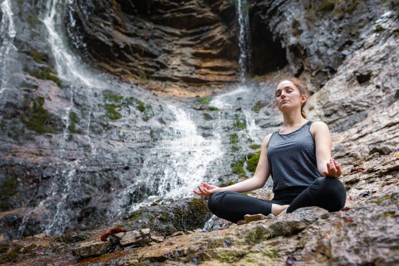 Woman Practicing Yoga, Sitting in Om Pose on the Rock Near a Waterfall ...