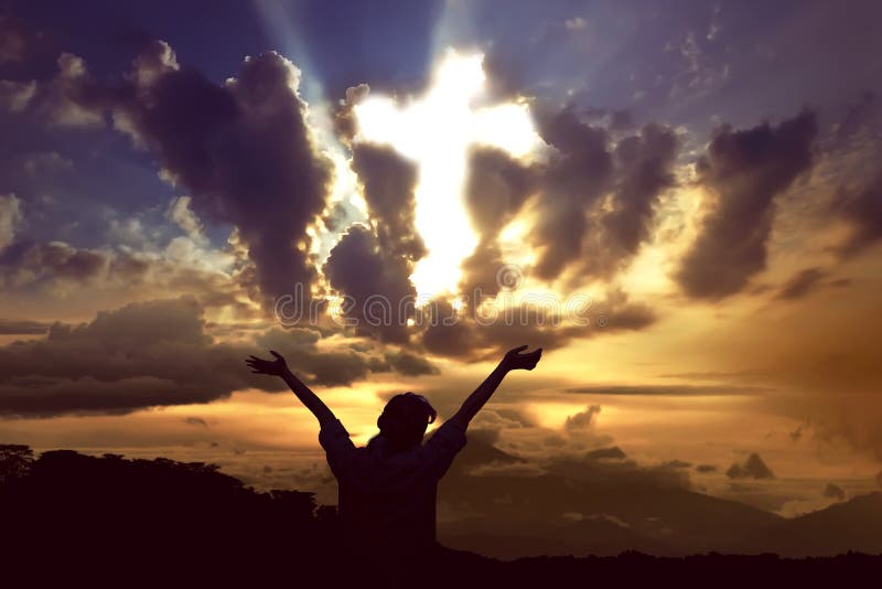 Woman praying to god with ray of light shaping cross on the sky