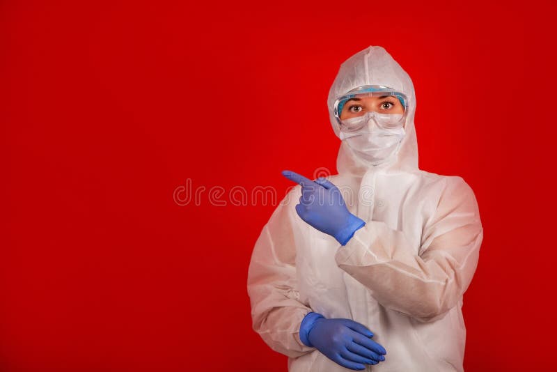 A woman in a protective suit against the COVID-19 virus indicates the direction. Medic woman wearing protective clothing against coronovirus on a red background