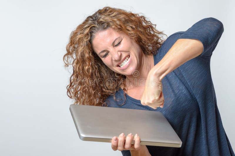 Middle aged Woman Showing Angry Face While punching her Laptop Computer Against White Background. Middle aged Woman Showing Angry Face While punching her Laptop Computer Against White Background.