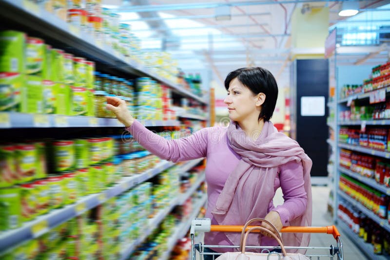 Woman pushing shopping cart choosing at goods in supermarket