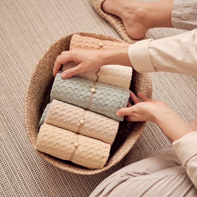 Woman puts in a wicker basket a composition of neatly rolled bathroom towels made of natural muslin. Natural, soft, air