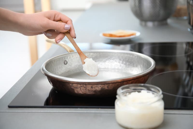 Woman putting coconut oil on frying pan in kitchen. 