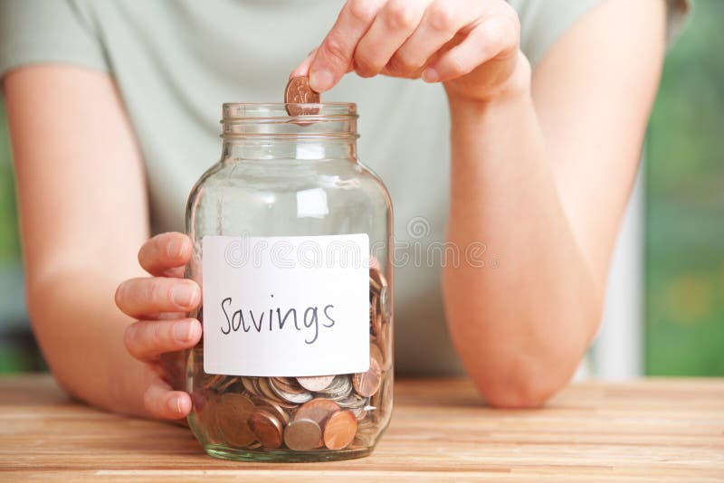 Woman Putting Coin Into Jar Labelled Savings