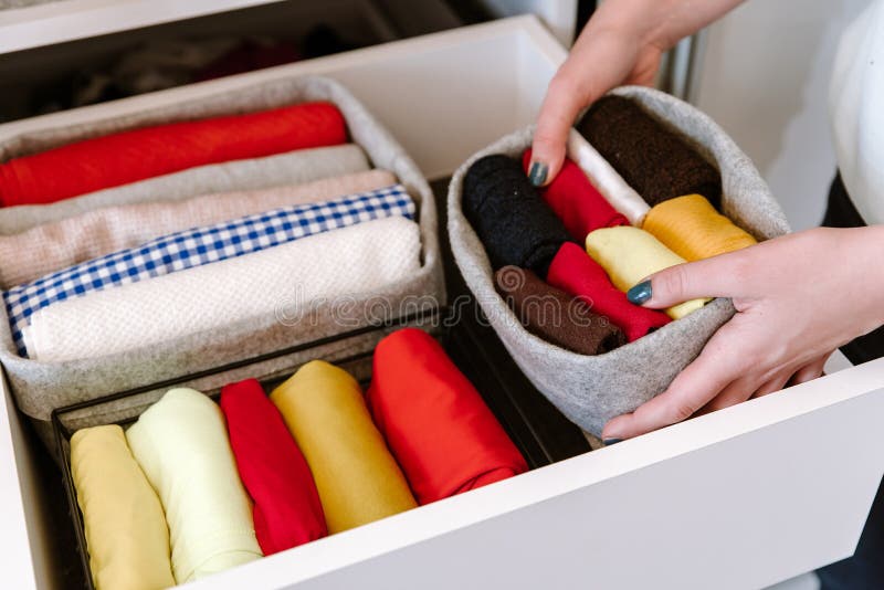 Woman organizing colorful clothes in wardrobe shelves. Minimalist closet