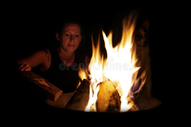 Woman putting more wood on the fire, camping and barbecue at night