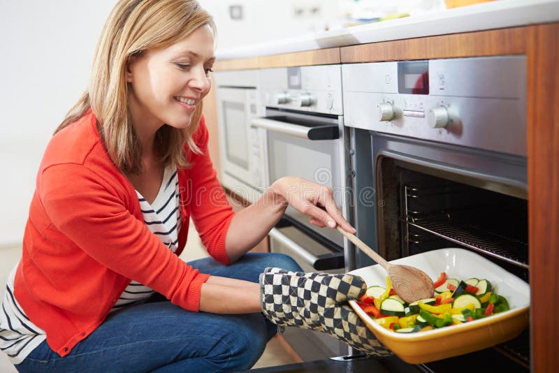 Woman Putting Tray Of Roast Vegetables Into Oven