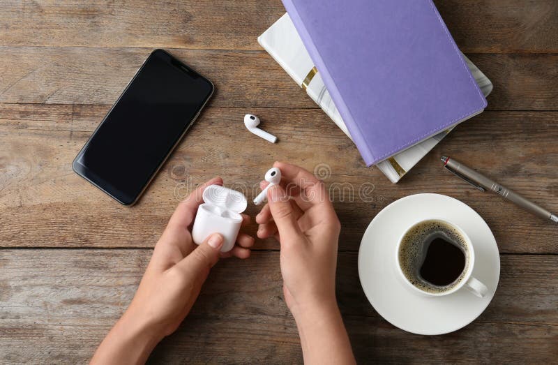 Woman putting wireless earphones in charging case at wooden table