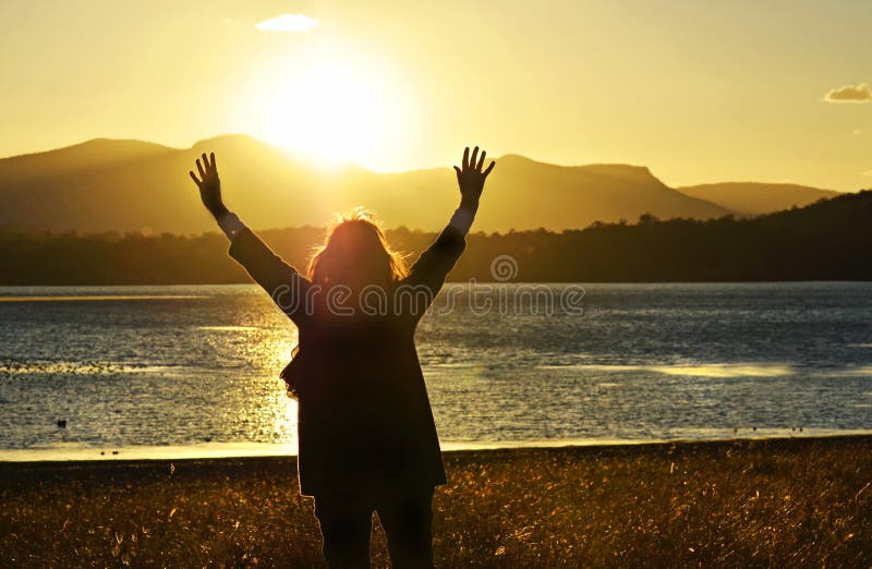 Woman raising hands worshiping praising praying God beautiful sunset