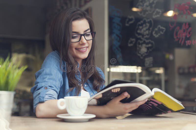 Sorridente donna che legge il giornale al bar.