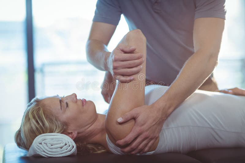 Professional female physiotherapist giving shoulder massage to blonde woman  stock photo