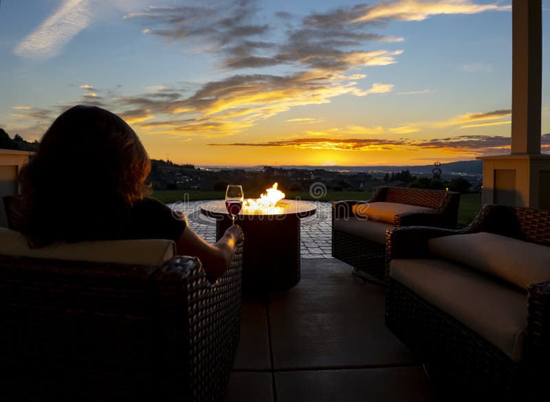 A woman relaxes with a glass of wine at night in front of an outdoor firepit on a patio of a luxury home overlooking a city. stock photography A woman relaxes with a glass of wine at night in front of an outdoor firepit on a patio of a luxury home overlooking a city. stock photography