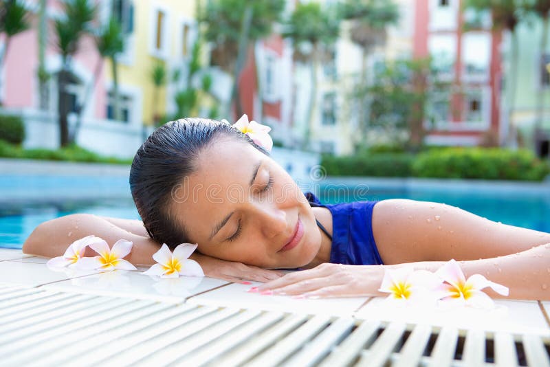 Woman relaxing with eyes closed by the side of swimming pool, flowers in hair
