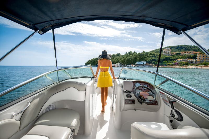 Junge hübsche Frau im gelben Badeanzug stehend auf der yacht schwimmt im Meer mit Blick auf die Insel.