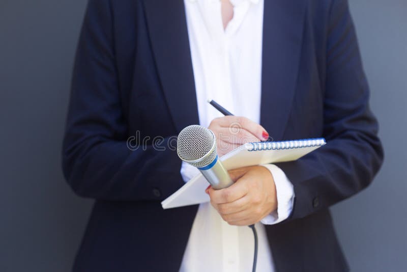 Woman reporter or journalist at media event, holding microphone, writing notes. Broadcast journalism concept.