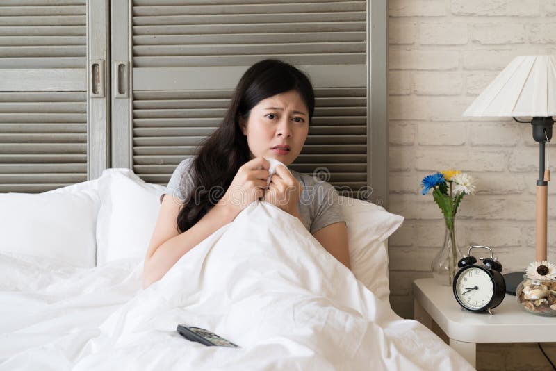 Asian woman retreat into her bed while she is watching the climax of whole movie. She is so nervous and expect to see the ending.