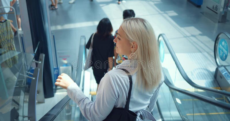 Woman ride down escalator. Back rear view. Escalator in shopping mall, woman slides down escalator to first floor