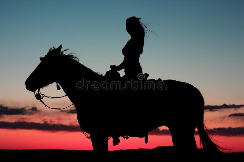 Silhouette di donna a cavallo di un cavallo in un bel tramonto nel deserto, con una leggera brezza che soffia i capelli.