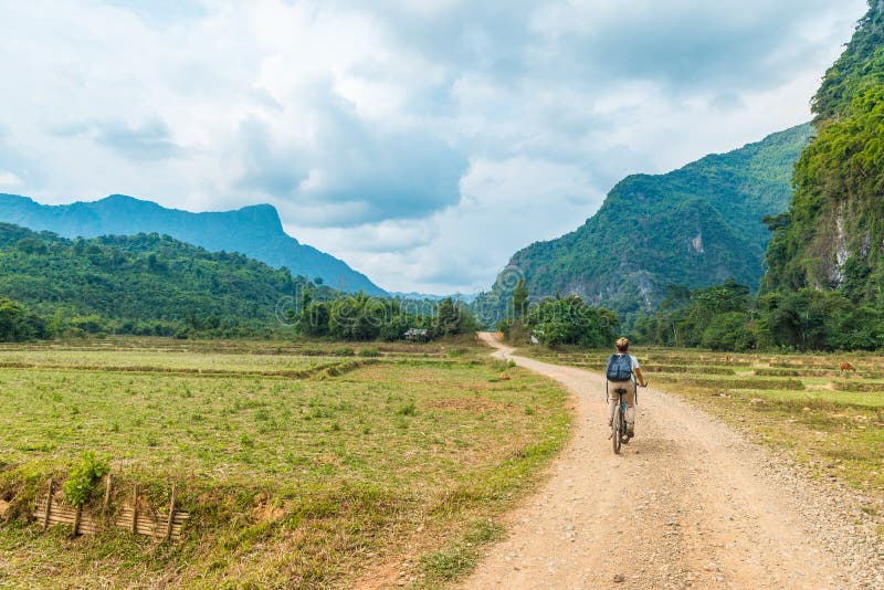 Woman riding mountain bike on dirt road in scenic landscape around Vang Vieng backpacker travel destination in Laos Asia rock stock photo Woman riding mountain bike on dirt road in scenic landscape around Vang Vieng backpacker travel destination in Laos Asia rock stock photo
