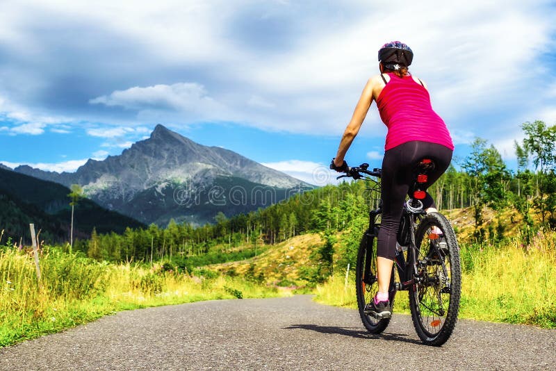 Žena na horském kole na silnici v lese s kopcem na pozadí ve Vysokých Tatrách, Slovensko